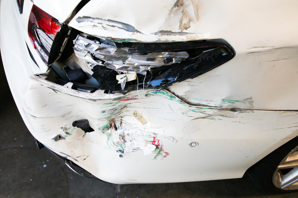 Das hintere Ende eines weißen Autos mit Dellen, Lackkratzern und kaputter Rückleuchte, geeignet für ein Kfz Schadengutachten