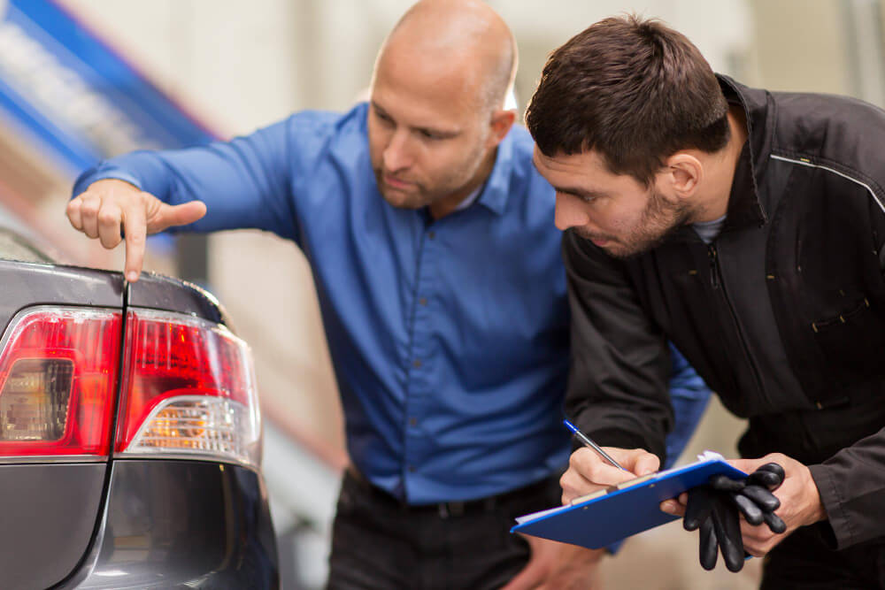 Zwei Männer begutachten das Heck eines Autos, einer zeigt auf das Rücklicht, der andere notiert Details für die Fahrzeugbewertung