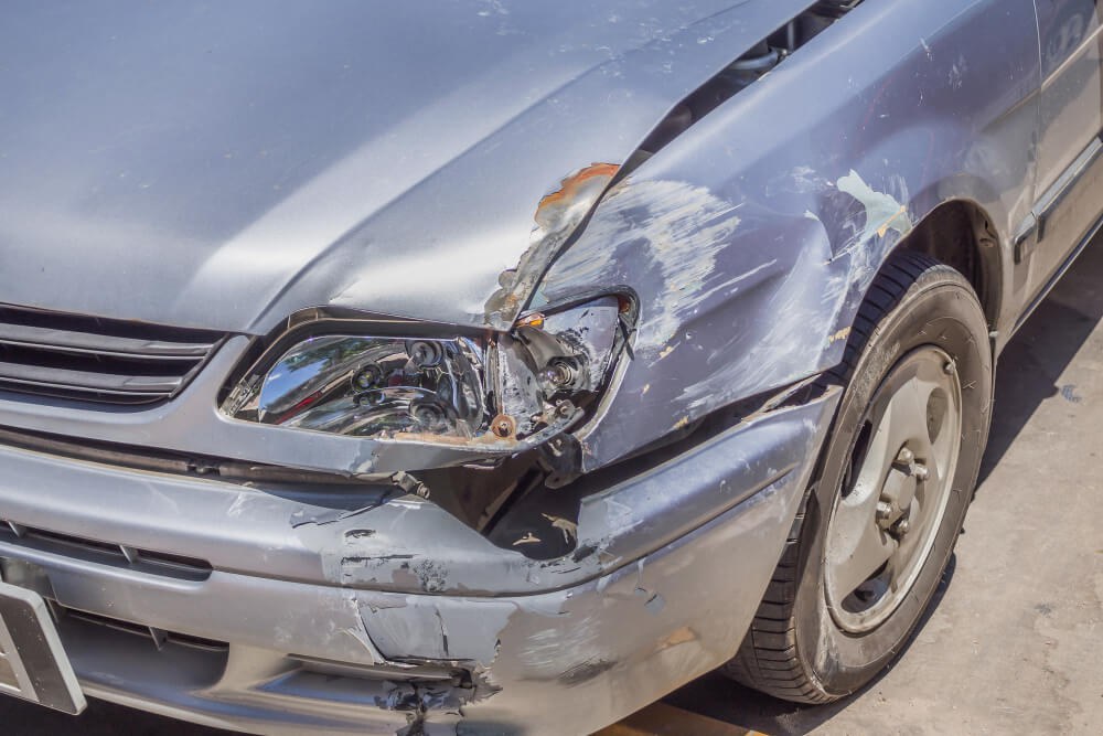 Ein silbernes Auto mit deutlichen Schäden am rechten vorderen Kotflügel, Stoßfänger und Scheinwerferbereich