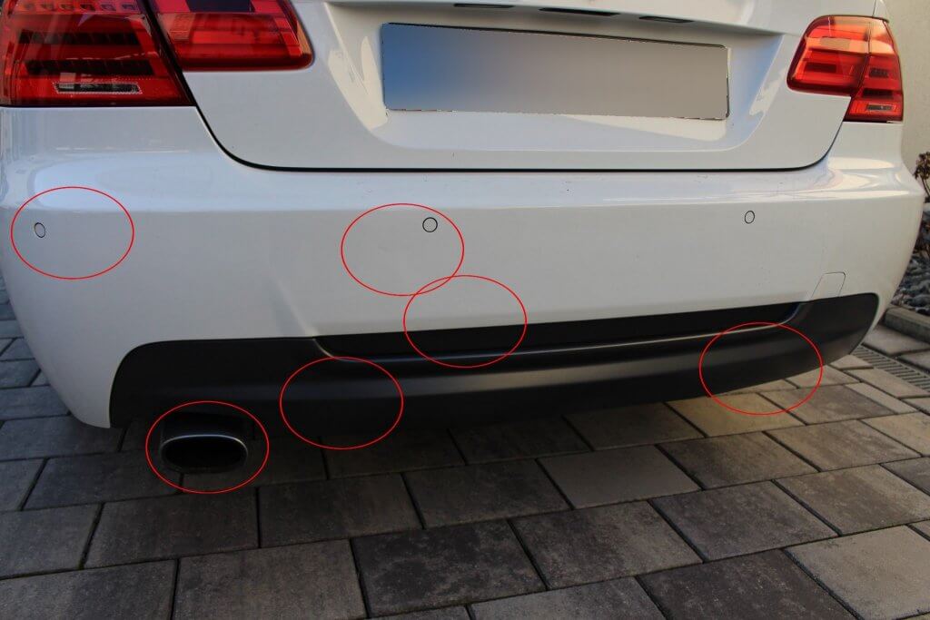 Nahaufnahme des hinteren Stoßfängers eines weißen Autos, wobei rote Kreise die Parksensoren markieren