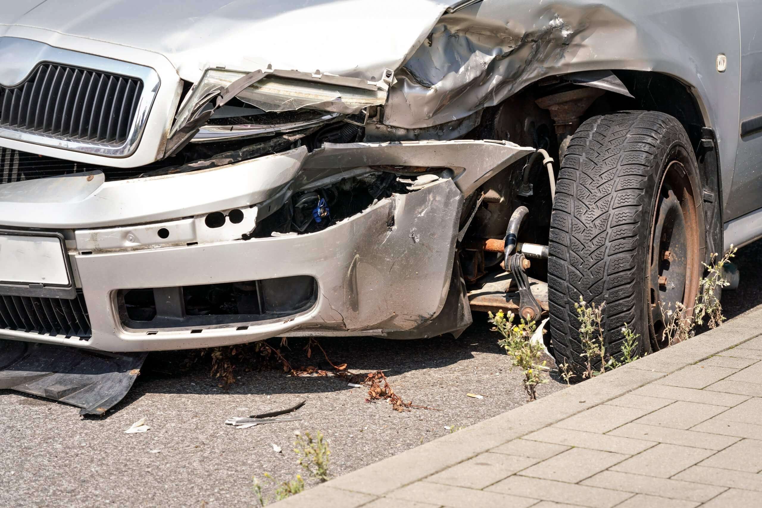 Nahaufnahme eines stark beschädigten silbernen Autos, automatisch gespeicherter Entwurf, mit zerbeulter Stoßstange und Rad am Bordstein