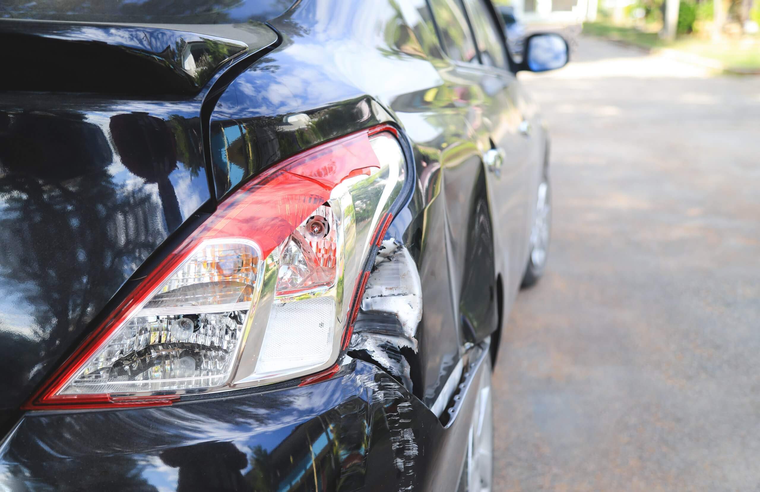 Nahaufnahme eines schwarzen Autos mit eingedrückter Heckseite, zerkratztem Lack und automatisch gespeichertem Entwurf bei Sonnenlicht