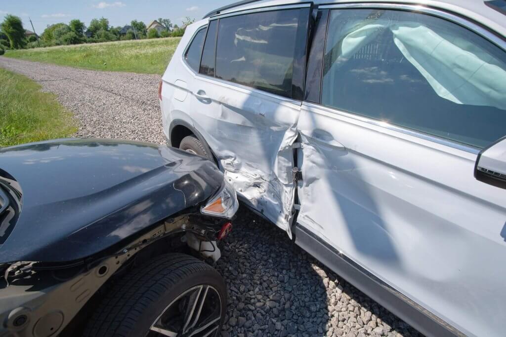 Ein schwarzes Auto und ein weißer SUV sind auf einer Schotterstraße zusammengestoßen, beide Fahrzeuge weisen starke Schäden auf