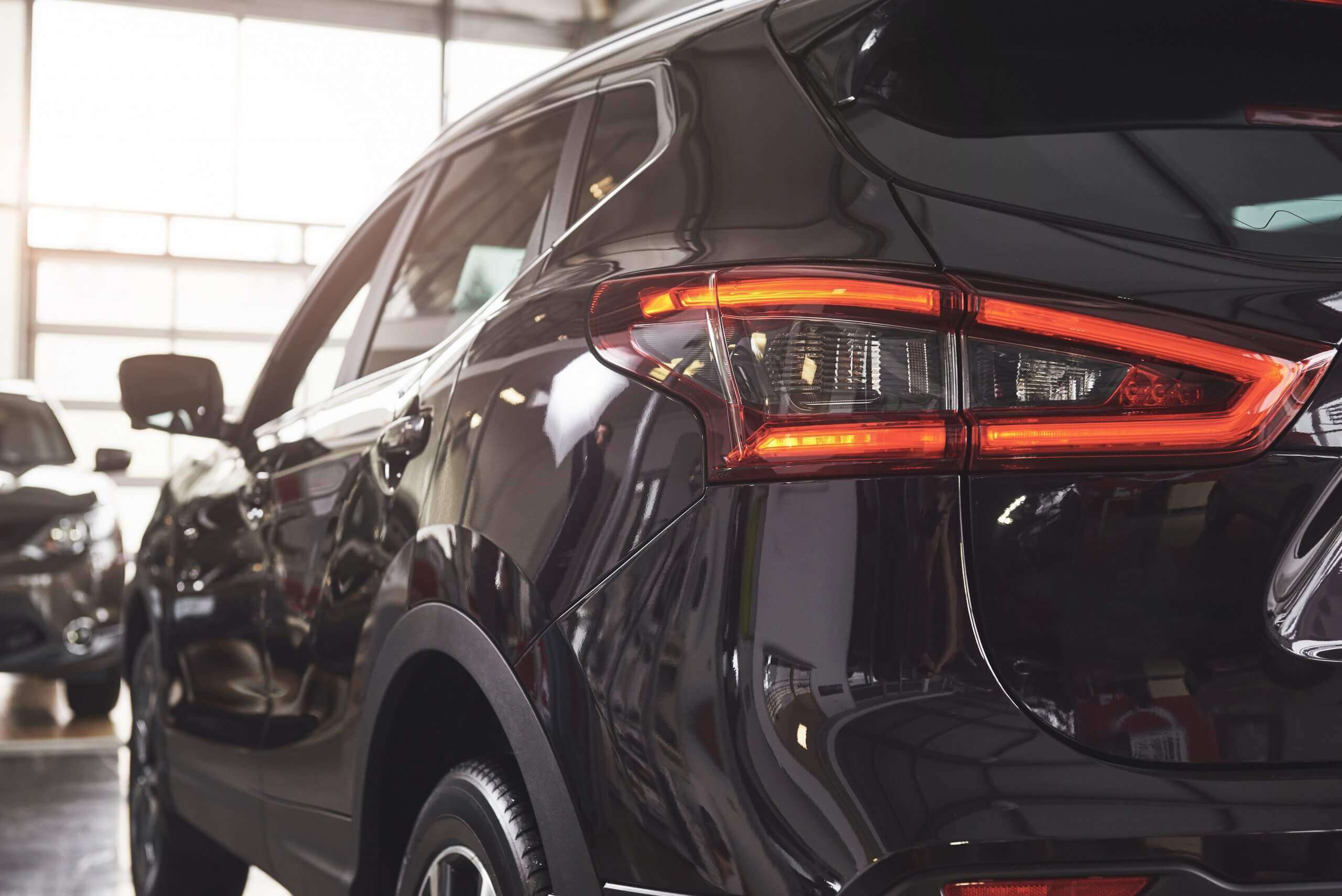 Das Heck und Rücklicht eines schwarzen SUVs, automatisch gespeicherter Entwurf, in einer Halle mit einfallendem Sonnenlicht