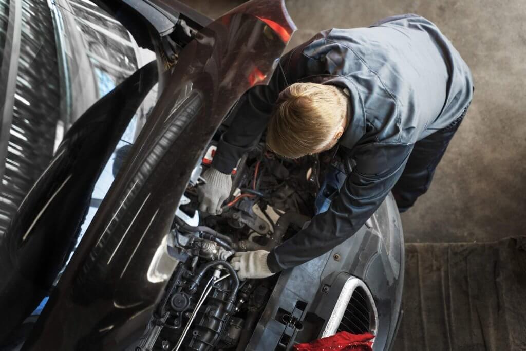 Ein Mechaniker mit Handschuhen repariert in einer Werkstatt einen Automotor, von oben betrachtet-ein automatisch gespeicherter Werkalltag-Entwurf