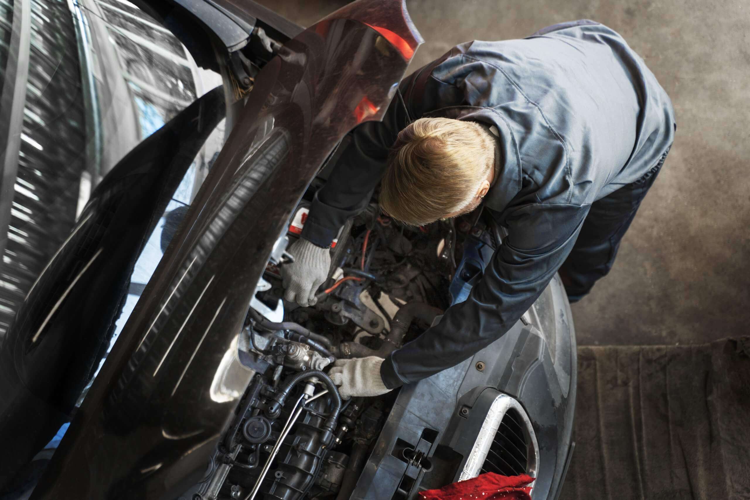 Ein Mechaniker mit Handschuhen repariert in einer Werkstatt einen Automotor, von oben betrachtet-ein automatisch gespeicherter Werkalltag-Entwurf