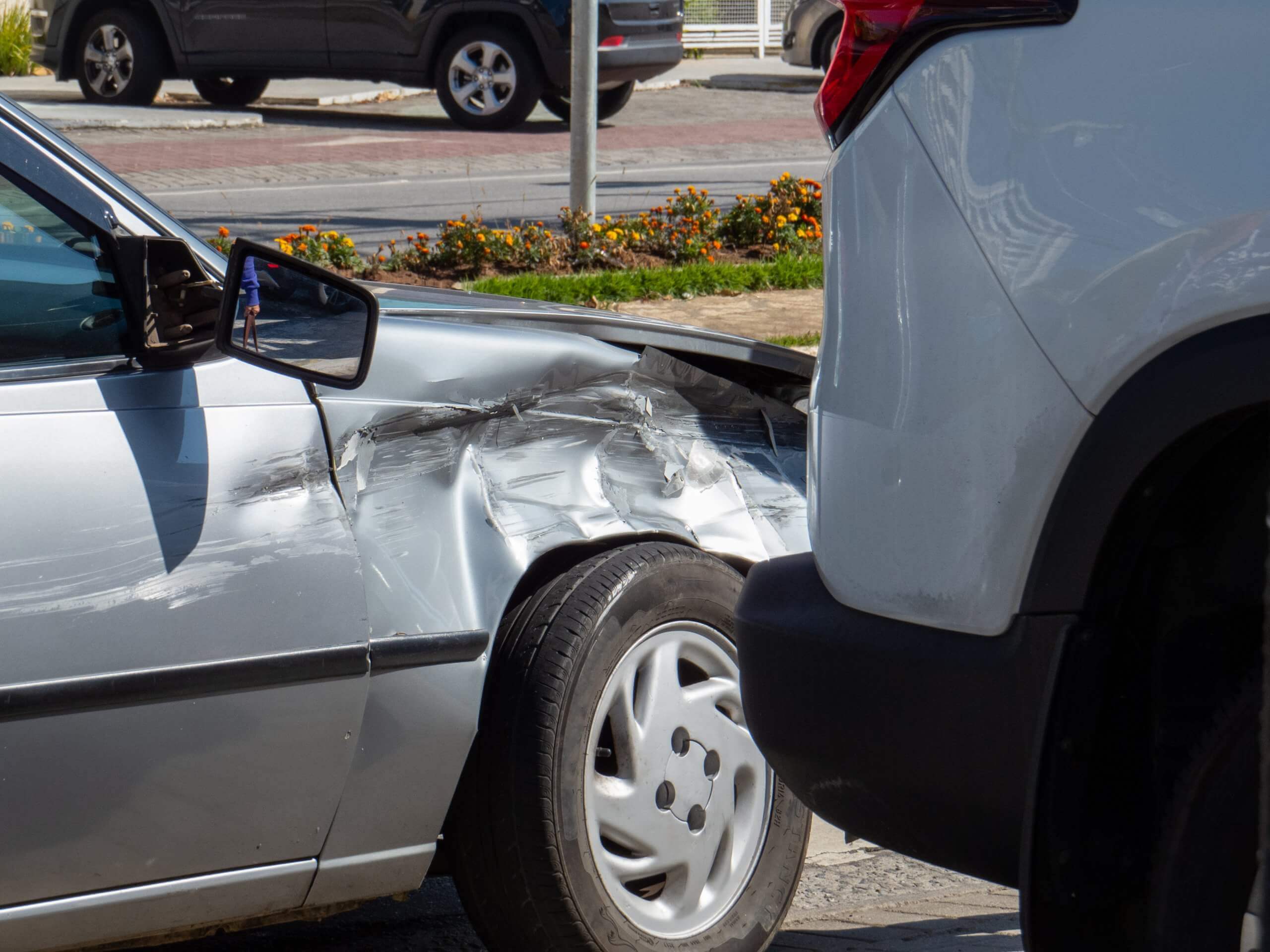 Ein silbernes Auto mit beschädigter Frontseite nach einem Unfall, als "Automatisch gespeicherter Entwurf" auf einer Stadtstraße markiert
