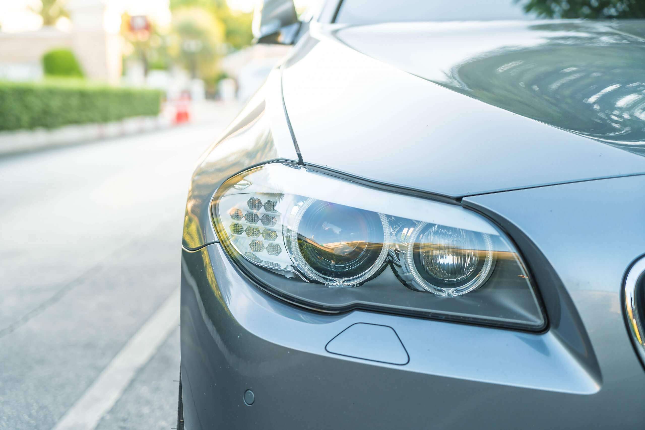 Das silberne Auto mit sichtbar linkem Frontscheinwerfer und Motorhaube steht tagsüber als automatisch gespeicherter Entwurf am Straßenrand