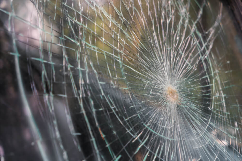 Nahaufnahme eines zerbrochenen Fensters mit sternförmig vom Einschlagpunkt ausgehenden Rissen, als wäre es ein automatisch gespeicherter Entwurf des Chaos