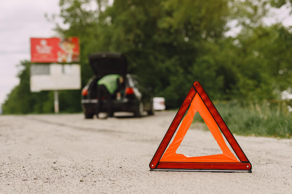 Ein Warndreieck auf der B4 bei Rötgesbüttel warnt vor einem Auffahrunfall; im Hintergrund ist ein Auto mit offenem Kofferraum zu sehen